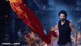 a man in a black tank top is holding a red cloth in front of flames and the words pranay varma on the bottom
