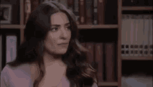 a woman is sitting in front of a bookshelf with her eyes closed and making a funny face .