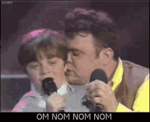 a man is singing into a microphone while a little girl kisses him on the cheek