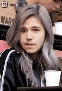 a man with gray hair and a beard is sitting at a table with a cup of coffee .