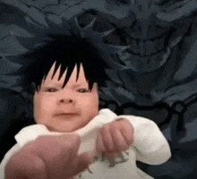 a baby with black hair is being held by a person and making a funny face .