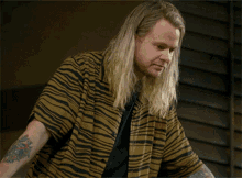 a man with long blonde hair and a tattoo on his arm is wearing a zebra print shirt