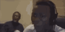 a man wearing headphones is making a funny face while another man looks on .