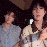 two young men are standing next to each other in a room and looking at the camera .