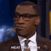 a man in a suit and tie is smoking a cigar and says meat freak huh .