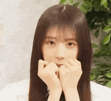 a close up of a young woman with long hair covering her mouth with her hands .