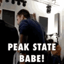 a man in a blue shirt is standing in a room with the words peak state babe .