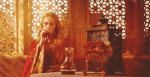 a woman is drinking from a glass while sitting at a table in front of a window .