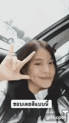 a woman is sitting in a car making a peace sign with her hand .