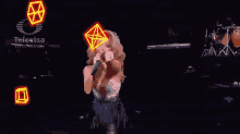 a woman singing into a microphone on a stage in front of a televisa logo
