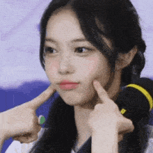 a young girl is touching her face with her fingers while holding a microphone in front of her .