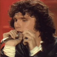 a close up of a man singing into a microphone with a red background