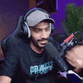 a man wearing headphones and a hat is talking into a microphone while sitting in a chair .