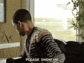 a man in a striped sweater is sitting on a couch and talking to someone .