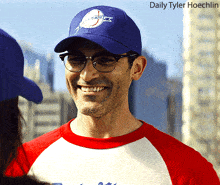 a man wearing glasses and a nasa hat smiles