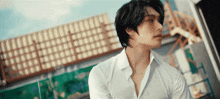 a man in a white shirt is standing in front of a building and looking away from the camera .