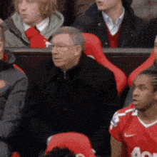 a man in a black jacket is sitting in a stadium with other people