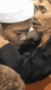 a man wearing a white hat is kissing another man 's forehead .