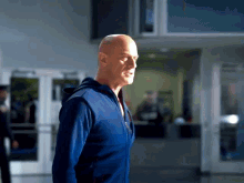 a bald man in a blue jacket stands in front of a door