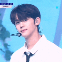 a young man wearing a tie and ear buds stands in front of a microphone with the words in bloom written above him