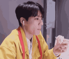 a young man in a yellow jacket is eating a sandwich