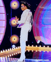 a woman in a white suit and white boots stands on a stage with lights behind her