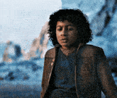 a young boy with curly hair is wearing a brown jacket with a star wars logo on it