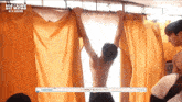 a shirtless man is hanging upside down from a curtain behind a sign that says 21f kiss