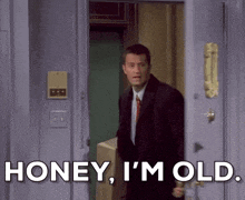 a man in a suit and tie is standing in a doorway and says honey i 'm old .