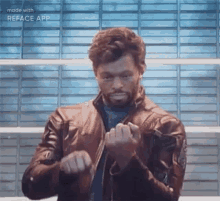 a man in a leather jacket is making a fist with his hands in front of a brick wall .