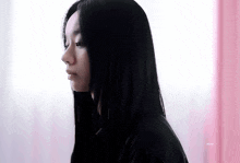 a woman with long black hair is standing in front of a pink wall