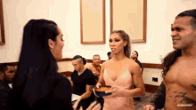 a woman in a pink dress is holding a bowl and talking to a man without a shirt