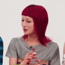 a woman with red hair and red nails is holding a bottle of water .
