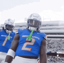 a football player wearing a blue jersey with the number 2 on it is standing next to another player wearing a white helmet .