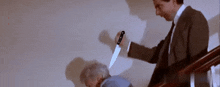 a man in a suit and tie is holding a knife over an older woman 's head