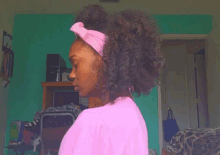 a woman wearing a pink shirt and a pink headband stands in front of a green wall