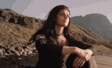 a woman is sitting on a rock in front of mountains