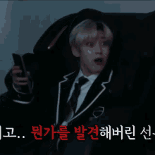 a man in a suit and tie is holding a cell phone with korean writing behind him