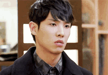 a young man wearing a black coat and a plaid shirt looks at the camera .