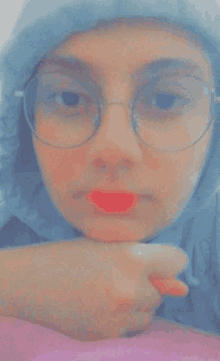 a girl wearing glasses and a hijab is taking a selfie with her hand on her chin .