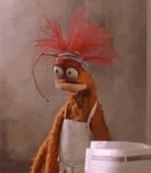 a stuffed animal with red hair and a white apron is standing next to a blender .