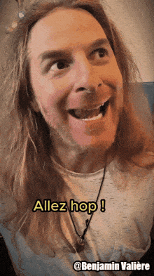 a man with long hair and a beard is smiling and says " allez hop "