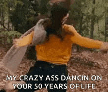 a woman in a yellow sweater is dancing in the woods with a man .