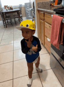 a little boy wearing a yellow hat is standing in a kitchen ..
