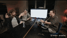 three men are sitting at a table with a laptop and a can of soda