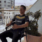 a man is sitting in a chair on a balcony with a tezos shirt on