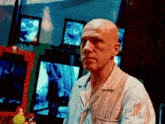 a bald man in a pajama shirt stands in front of a row of televisions