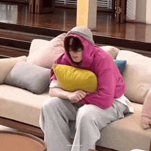 a man in a pink hoodie is sitting on a couch with a yellow pillow .