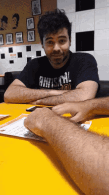 a man wearing a shirt that says antisocial sits at a table with his arms crossed