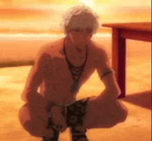 a shirtless man is squatting down on the beach .